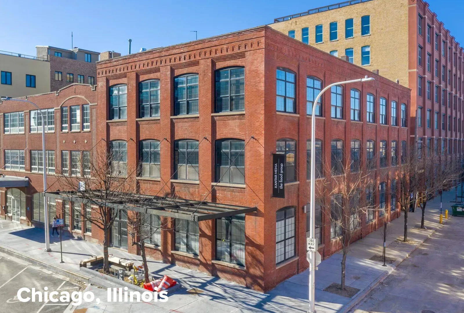 Red brick mixed-use building with tall arched windows on multiple floors along a tree-lined city street, Chicago, Illinois, on a sunny day.